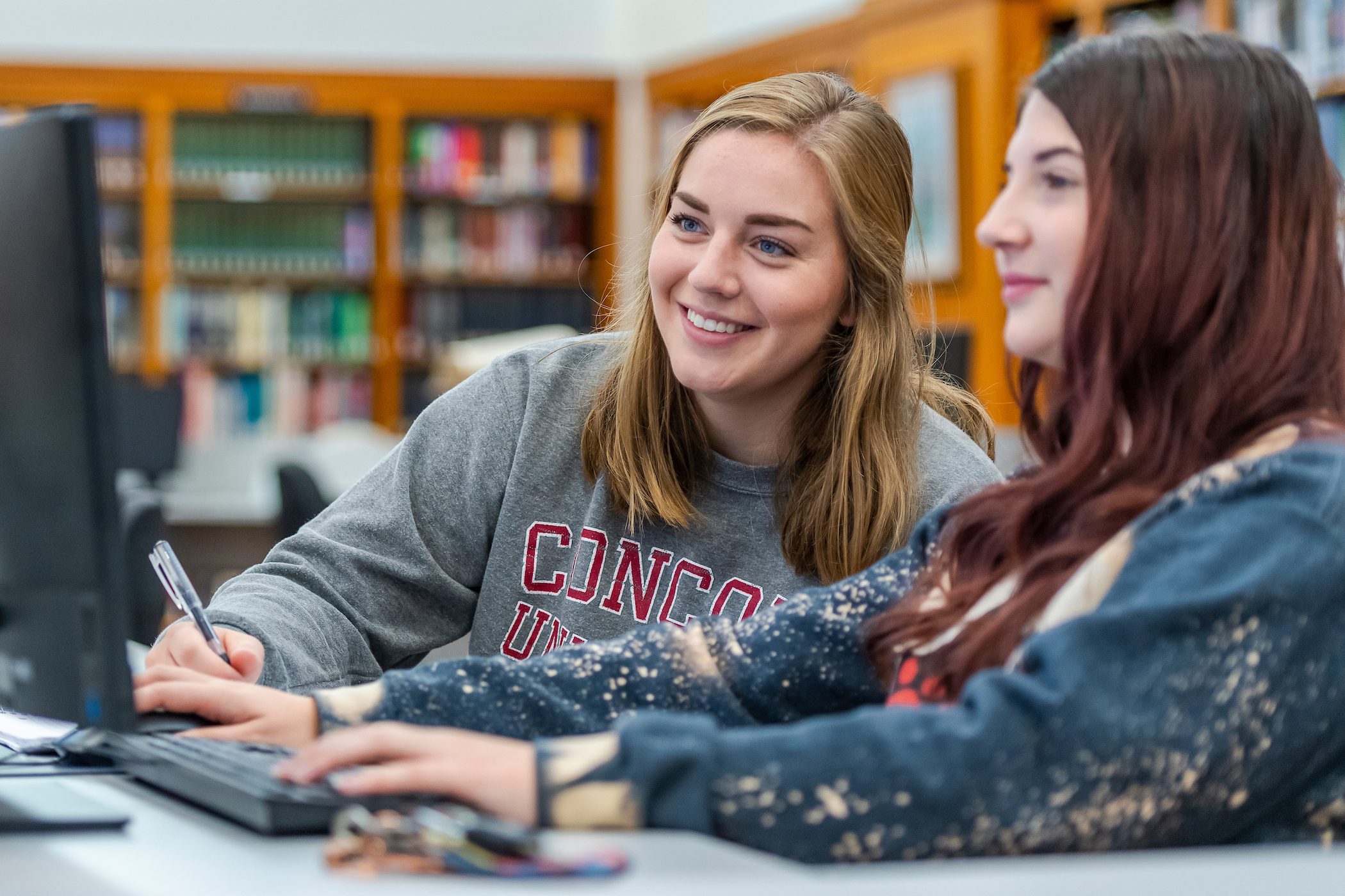 Two students working together on an assignment in the library