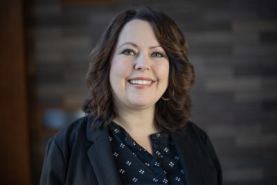 A photo of Andrea Sullivan in front of a gray slate wall