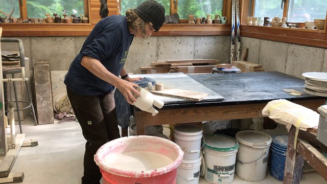 A photo of Linda Christianson, the guest artist for the 2024 WV Potters' Gathering, working on a piece in her studio