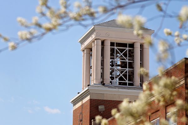 A photo of Concord University's bell tower with white flowers in the foreground and a clear blue sky in the background